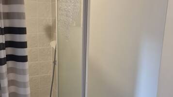A shower enclosure with a frosted glass door, a handheld showerhead, and a shower control panel.