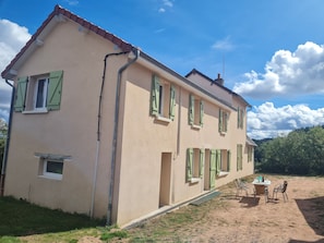 Un bâtiment à deux étages doté de nombreuses fenêtres, d’un petit espace extérieur aménagé avec une table et des chaises, et d’un système de drainage visible.