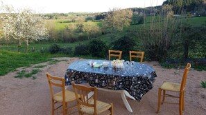 Un espace extérieur aménagé pour les repas, avec une table ronde, quatre chaises et une nappe à motifs.