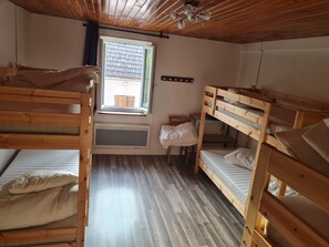 Una stanza con letto a castello, finestra, soffitto in legno e termosifone.