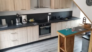 A modern kitchen with light wood cabinets, a black countertop, stainless steel appliances, and a wooden table with glasses.