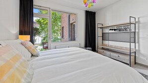 A bedroom with a large bed, a window with curtains, a radiator, a hanging light fixture, and a built-in wardrobe with shelves. - Central & luminous apartment in Antwerp, foreseen with all comforts (Antwerpen)