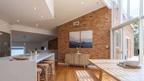 Una cocina moderna con pared de ladrillo, taburetes de madera y una isla grande con un fregadero y utensilios de bar.