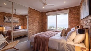 Un dormitorio con pared de ladrillo, un ventanal grande, una cama, una silla y un ventilador de techo.