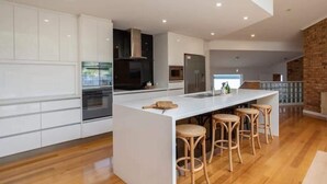 Una cocina moderna con armarios blancos, una isla central con taburetes, una pared de acento de ladrillo e iluminación empotrada.
