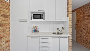 A kitchen with white cabinets, a microwave, a sink, and a brick wall. - 'Hillside Studio' self-contained with City Views. (Howrah)