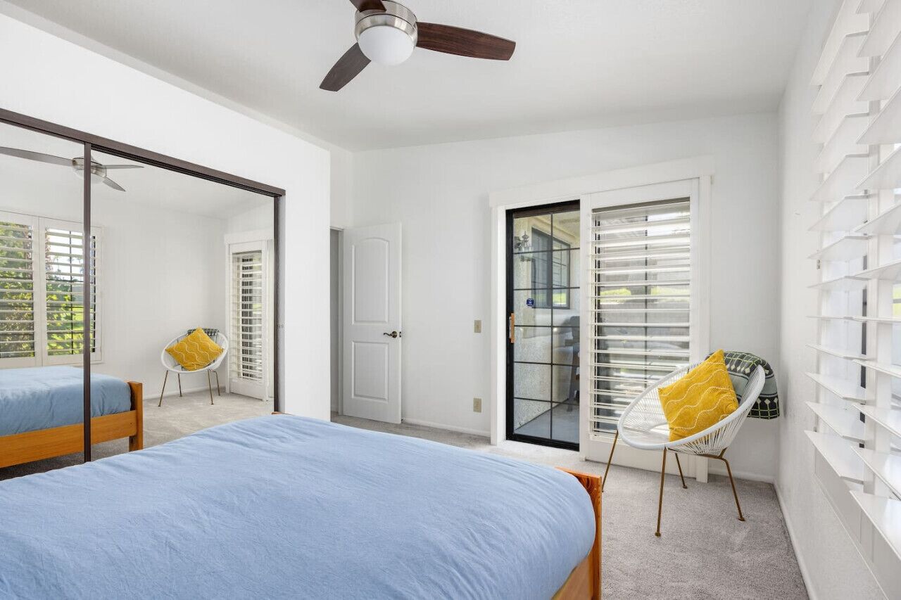 Une chambre avec deux lits, un ventilateur de plafond, une porte-fenêtre coulissante et une étagère blanche.
