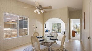 Un coin repas avec une table ronde en verre, des chaises en osier blanches et un ventilateur de plafond.