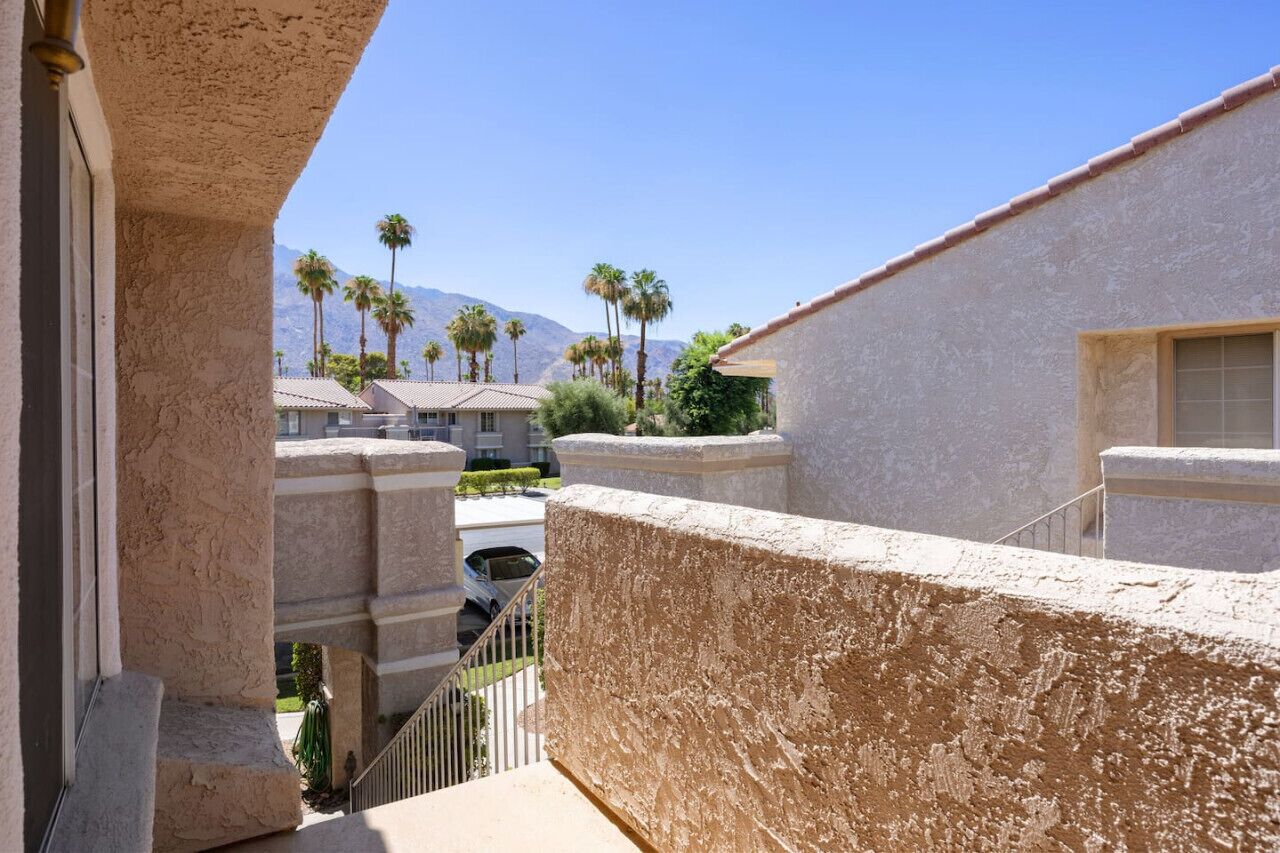 A view from a balcony overlooking a residential area with palm trees and mountains in the background.