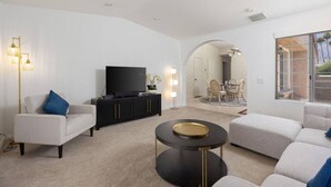 Un salon moderne doté d’un téléviseur à écran plat, d’un canapé, d’une table basse et d’un coin repas visible à travers une arche.