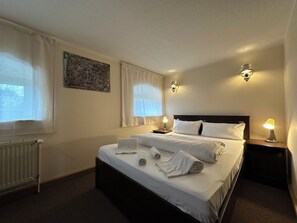 A neatly made bed with white linens, two bedside lamps, and a radiator on the wall.