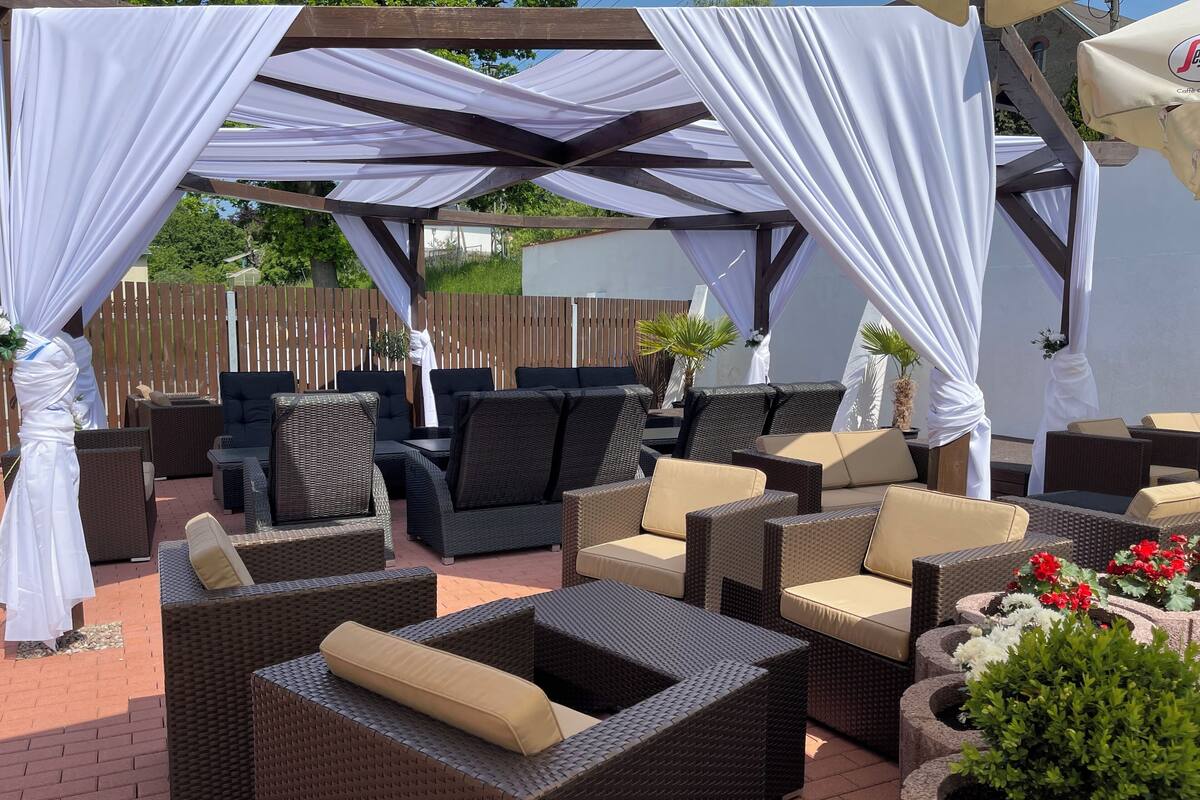 An outdoor patio with wicker furniture, white drapes, and potted plants.