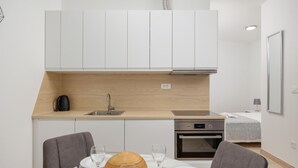 A compact kitchen with white cabinets, a wooden countertop, a built-in oven, and a dining area with a table set for two. - Awesome apartment in Podstrana with WiFi (Podstrana)