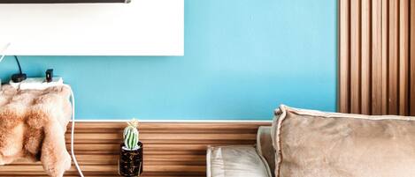 A room with a TV mounted on a wall, a wooden slat design, a teal accent wall, a sofa, and two potted plants.