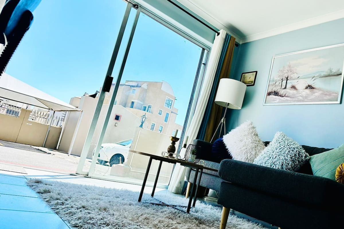Ein modernes Wohnzimmer mit einer Couch, einem Couchtisch und einem großen Fenster mit Blick auf Gebäude und ein parkendes Auto.