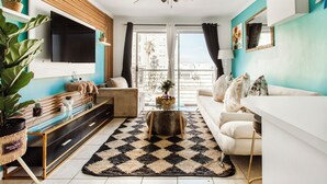 A modern living room with a TV, sofa, coffee table, and large windows. - Caline VIP Beach Close (Cape Town)