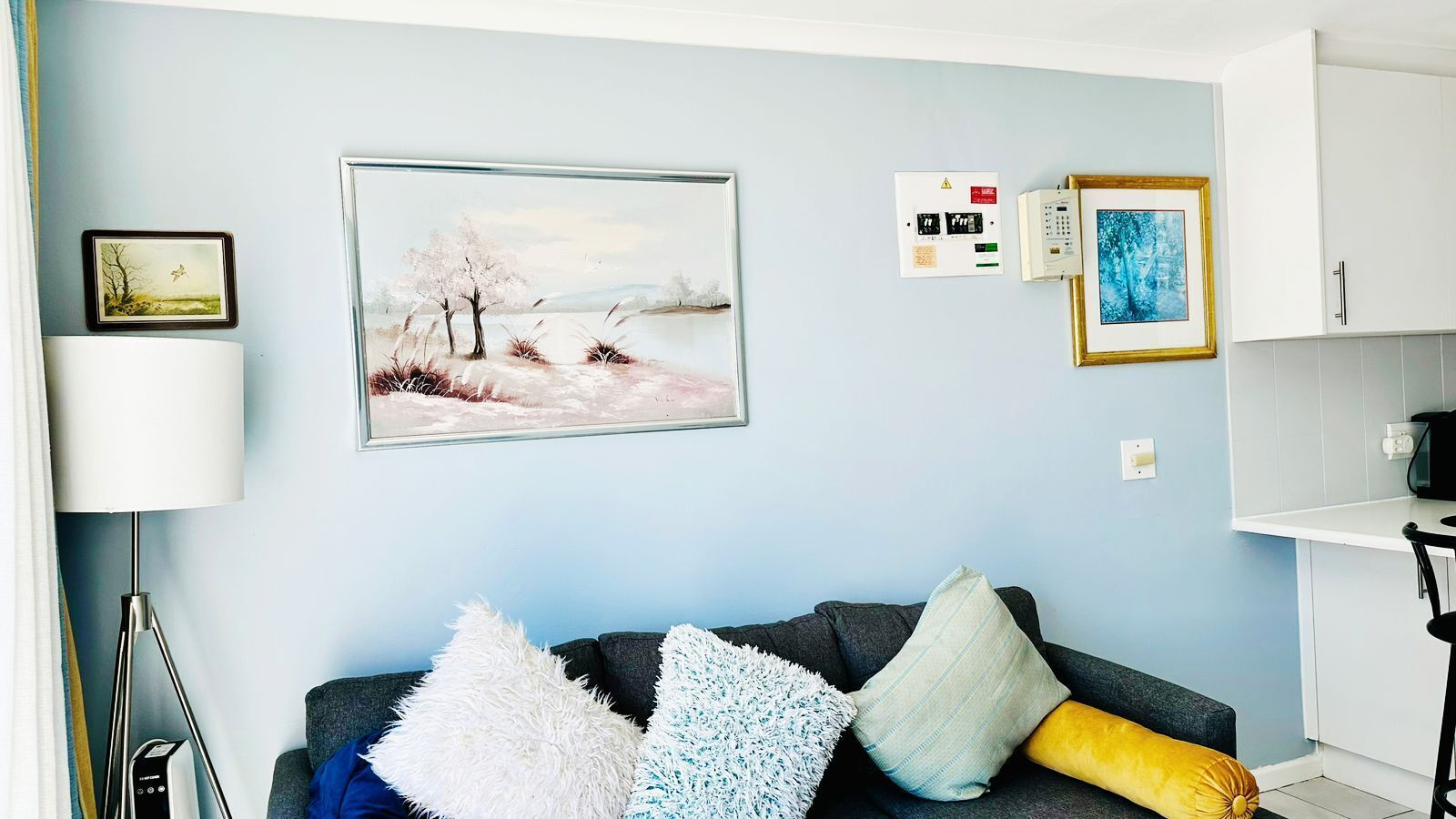 Ein Wohnzimmer mit einem dunkelgrauen Sofa, einer weißen Lampe und einem gerahmten Landschaftsbild.