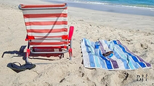 A beach chair with a striped towel and flip-flops on the sand, with a mountain in the background. - Caline VIP Beach Close (Cape Town)