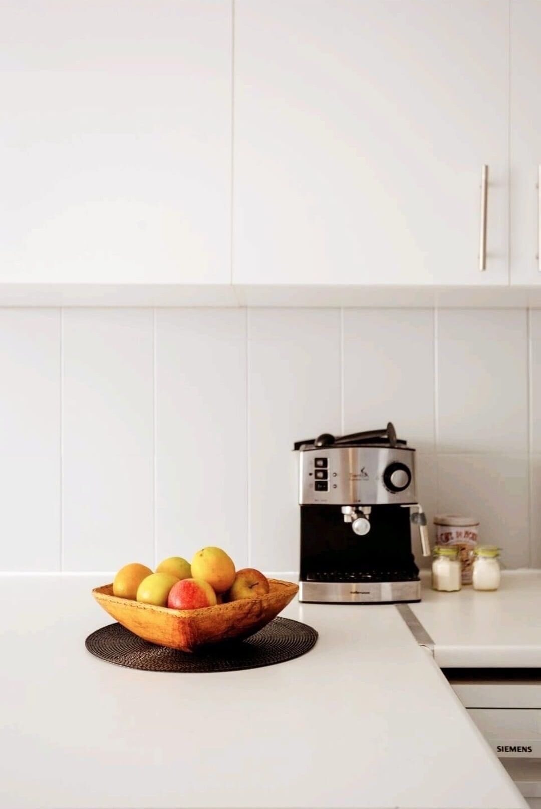 A kitchen with a coffee machine, a bowl of fruit, and a Siemens refrigerator.