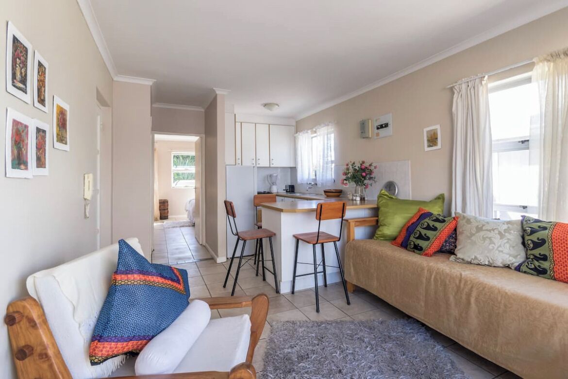 A cozy living room with a sofa, a coffee table, and a dining area with chairs and a kitchen in the background.