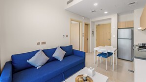 Een moderne woonkamer met een blauwe bank, een eettafel en een keuken met een koelkast.