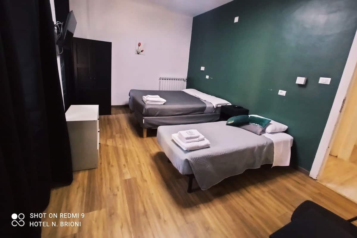 A room with two beds, a radiator, a small table, and a wall-mounted light fixture.