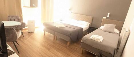 A hotel room with two beds, a desk, a chair, and a small table.