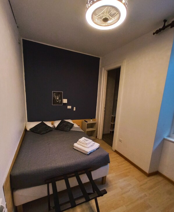 A small, modern bedroom with a bed, a bedside table, a wall-mounted light fixture, and a door leading to another room. - Albergo N. Brioni (Trieste)