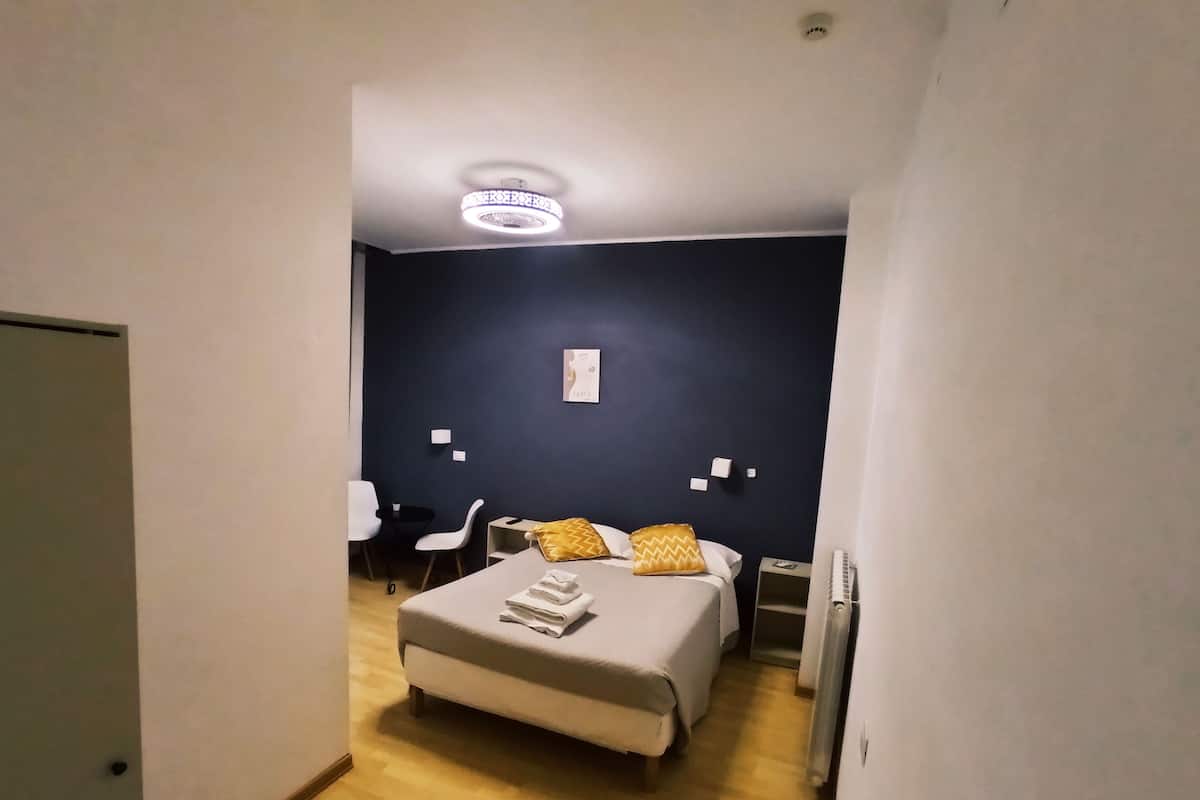 A modern hotel room with a bed, bedside tables, a desk, and a chair.