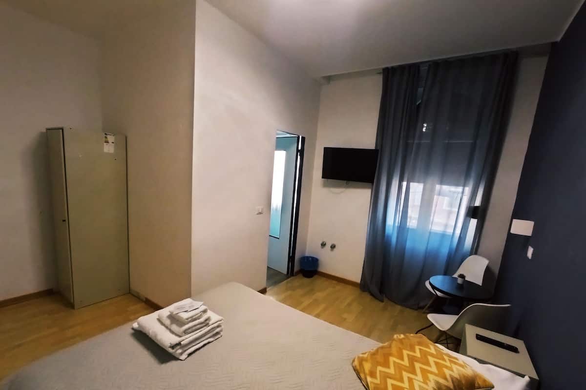 A hotel room with a bed, a desk, a chair, a television, and a wardrobe.