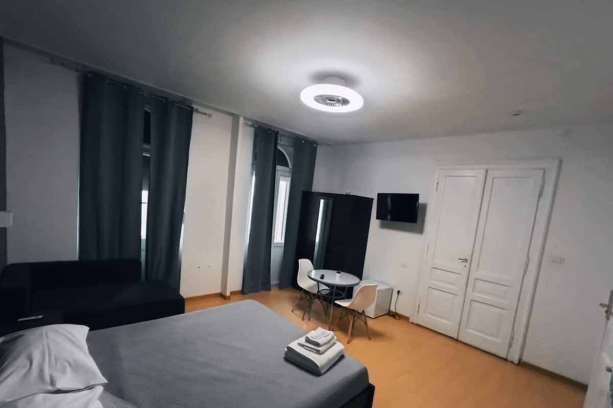 A hotel room with a bed, a desk, a chair, a TV, and a door.