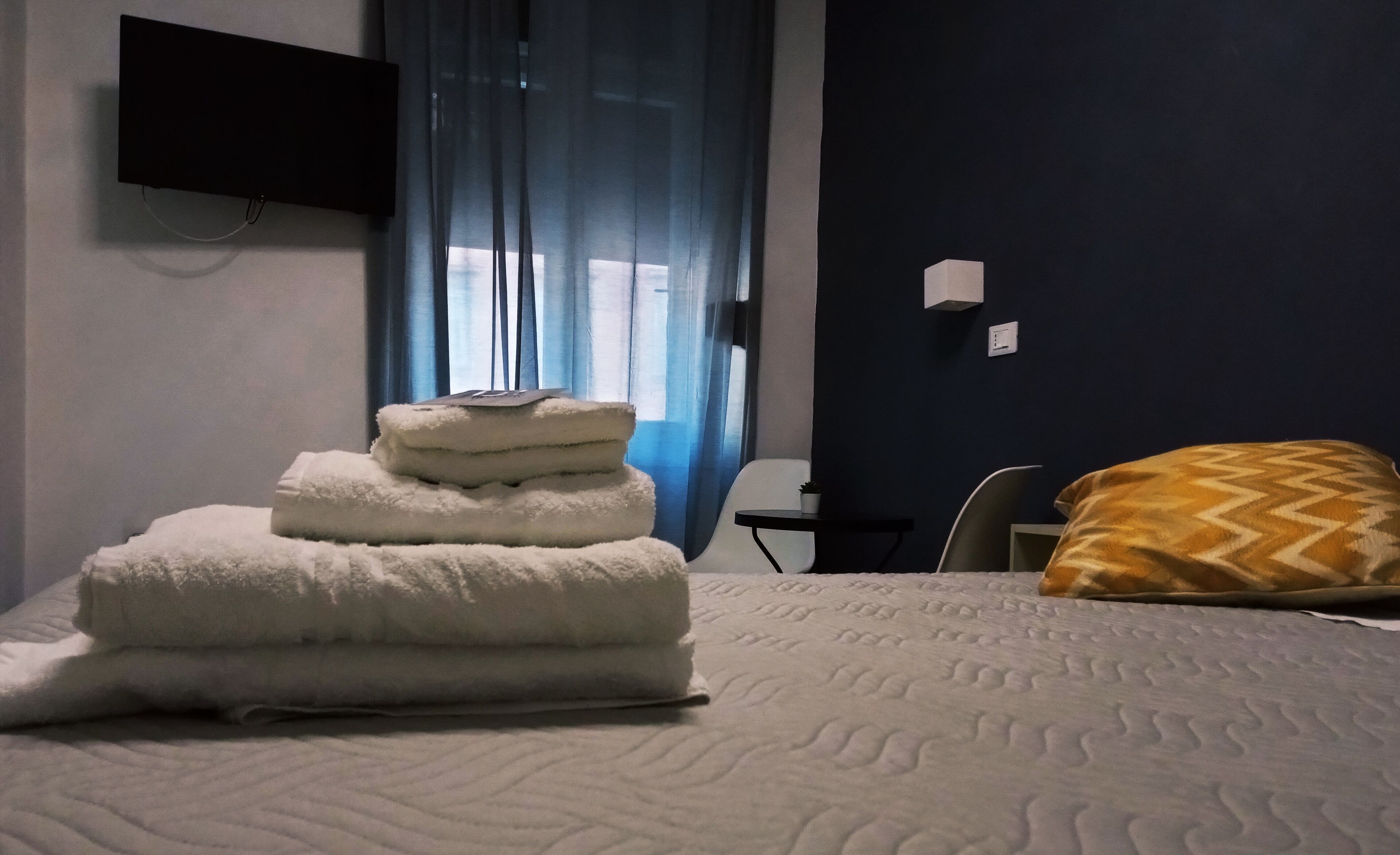A hotel room with a bed, a TV mounted on the wall, a desk, and a chair.