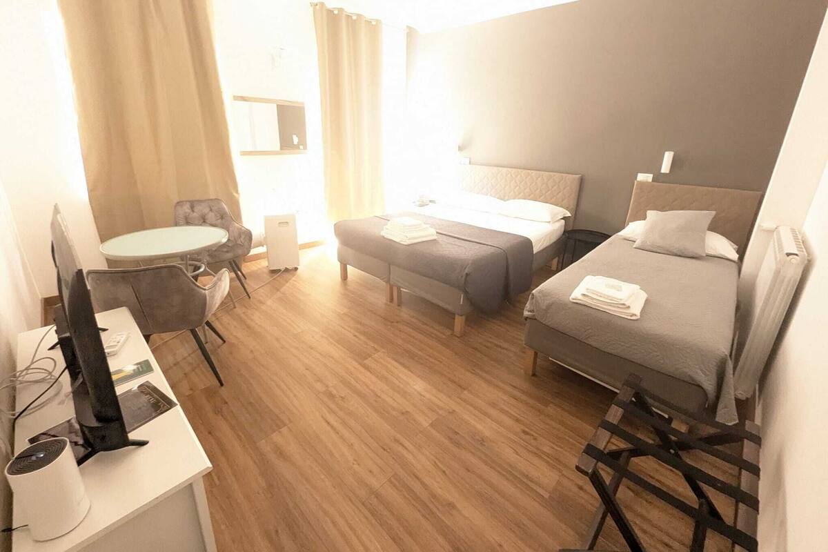 A hotel room with a bed, a desk with a computer, a chair, and a small table.