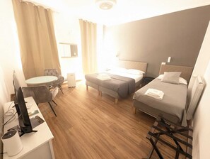 A hotel room with a bed, a desk with a computer, a chair, and a small table. - Albergo N. Brioni (Trieste)