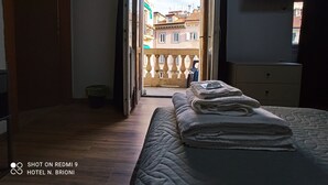 A hotel room with a bed, a dresser, and a view of buildings through an open door. - Albergo N. Brioni (Trieste)