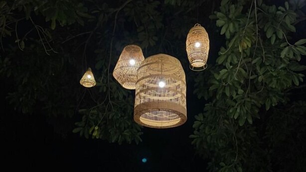 Des luminaires d’extérieur, une structure en chaume et des meubles en osier.