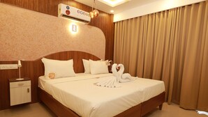 Une chambre d’hôtel avec une tête de lit en bois, un lit avec du linge de lit blanc, une table de chevet et un climatiseur fixé au mur.