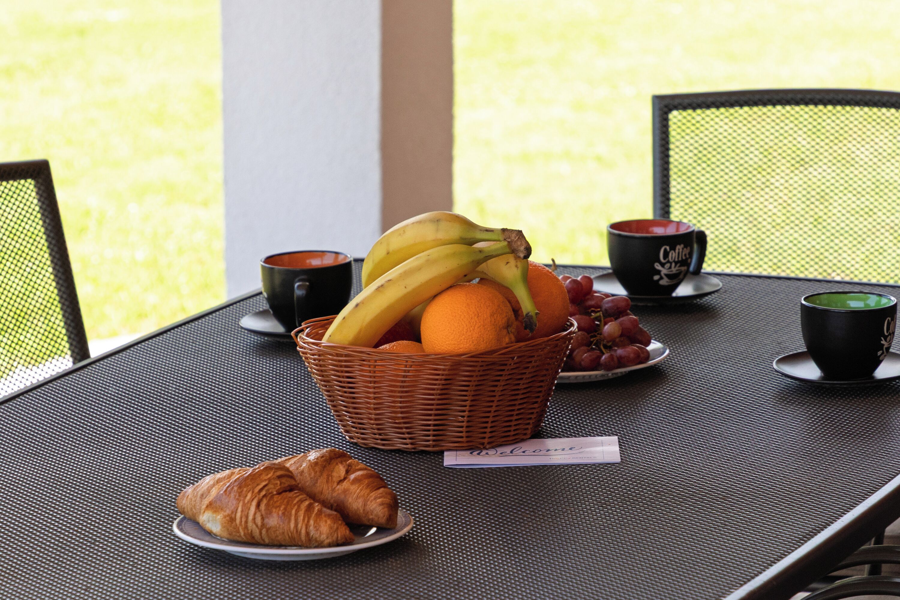 Pöydällä on hedelmäkori, kaksi kahvikuppia, croissant ja tervetulotoivotus.