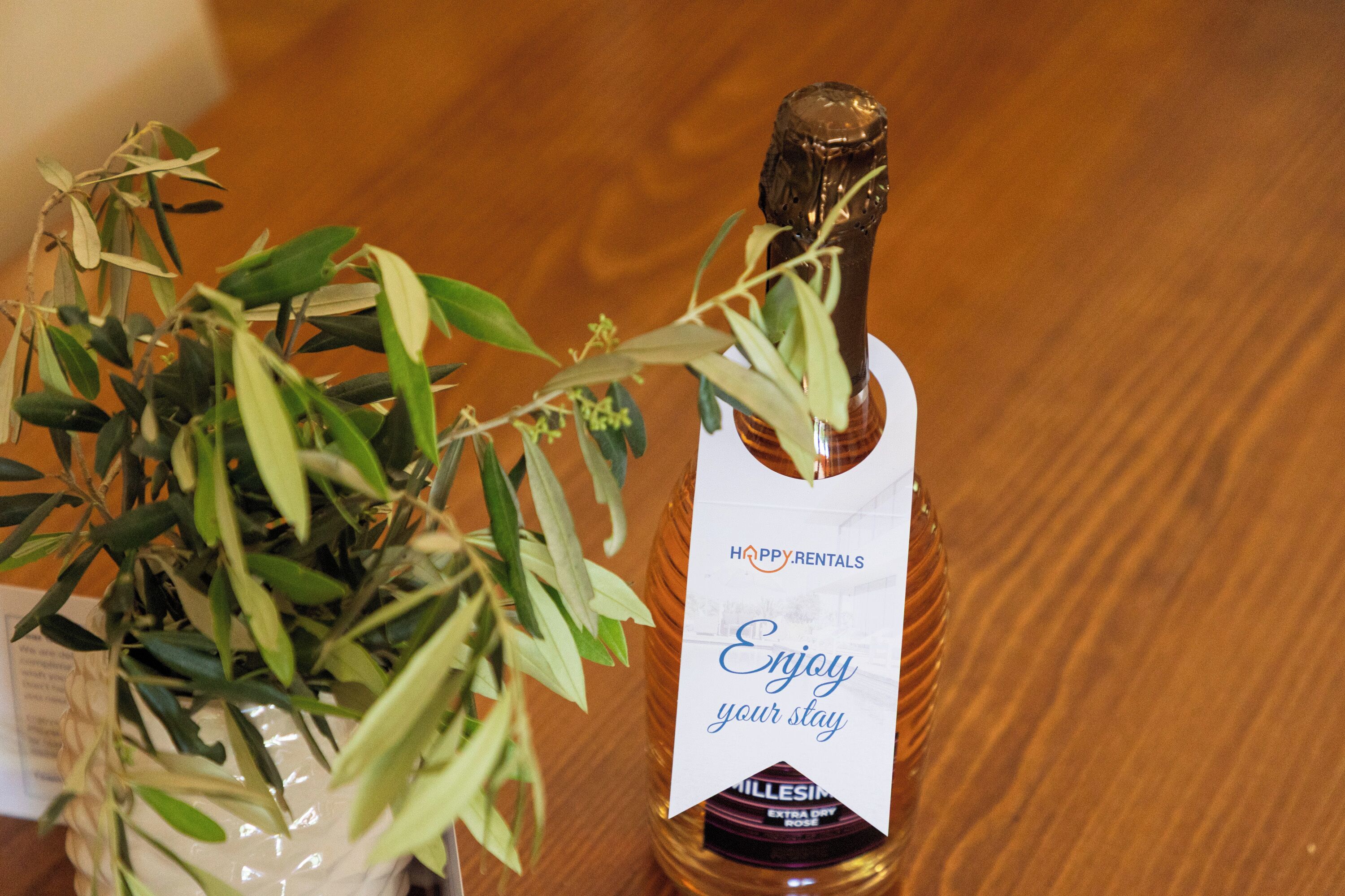 Una botella de champán con una etiqueta que dice 'Disfrute de su estancia' y una planta a su lado.