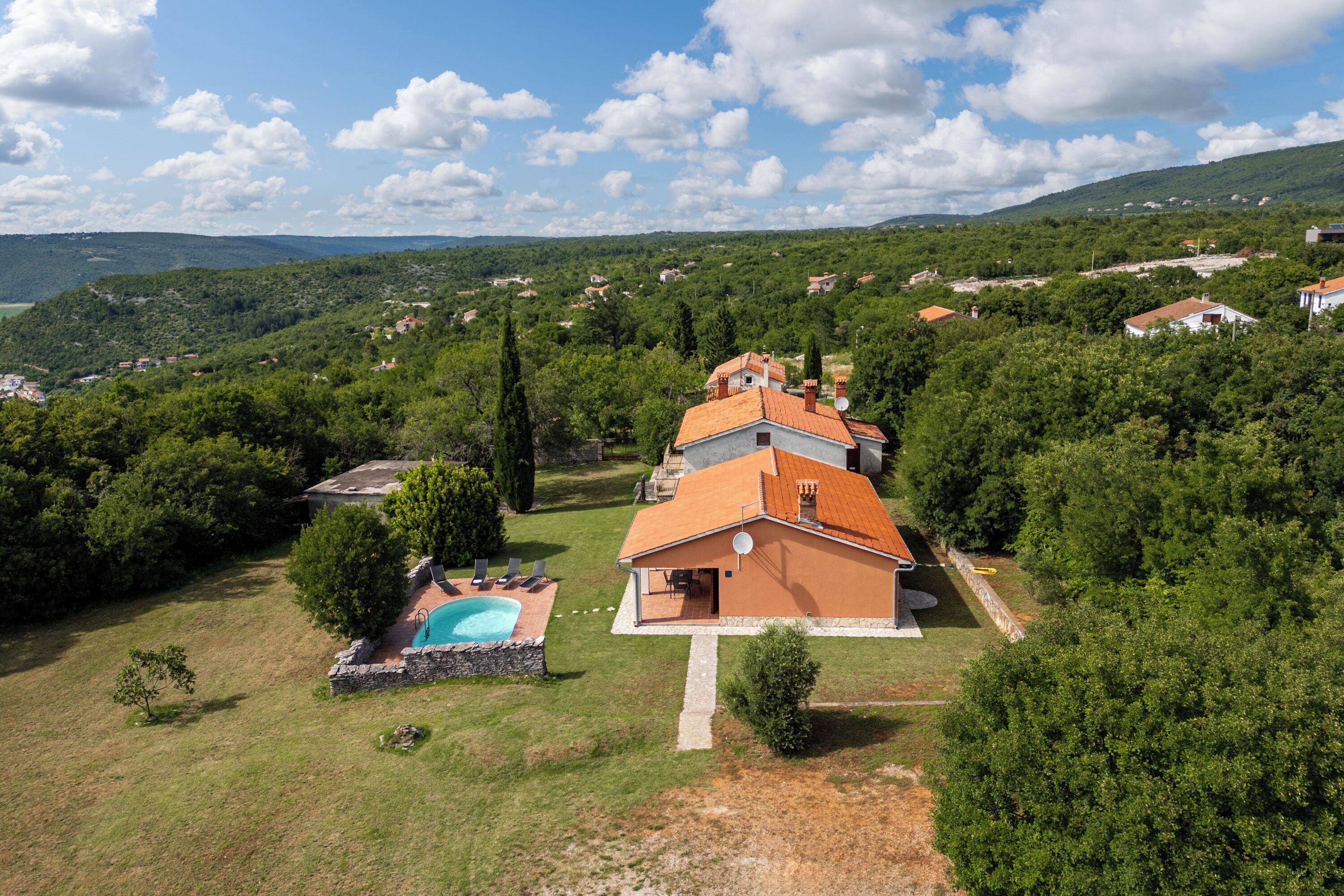 A house with a swimming pool, surrounded by lush greenery and hills in the background.