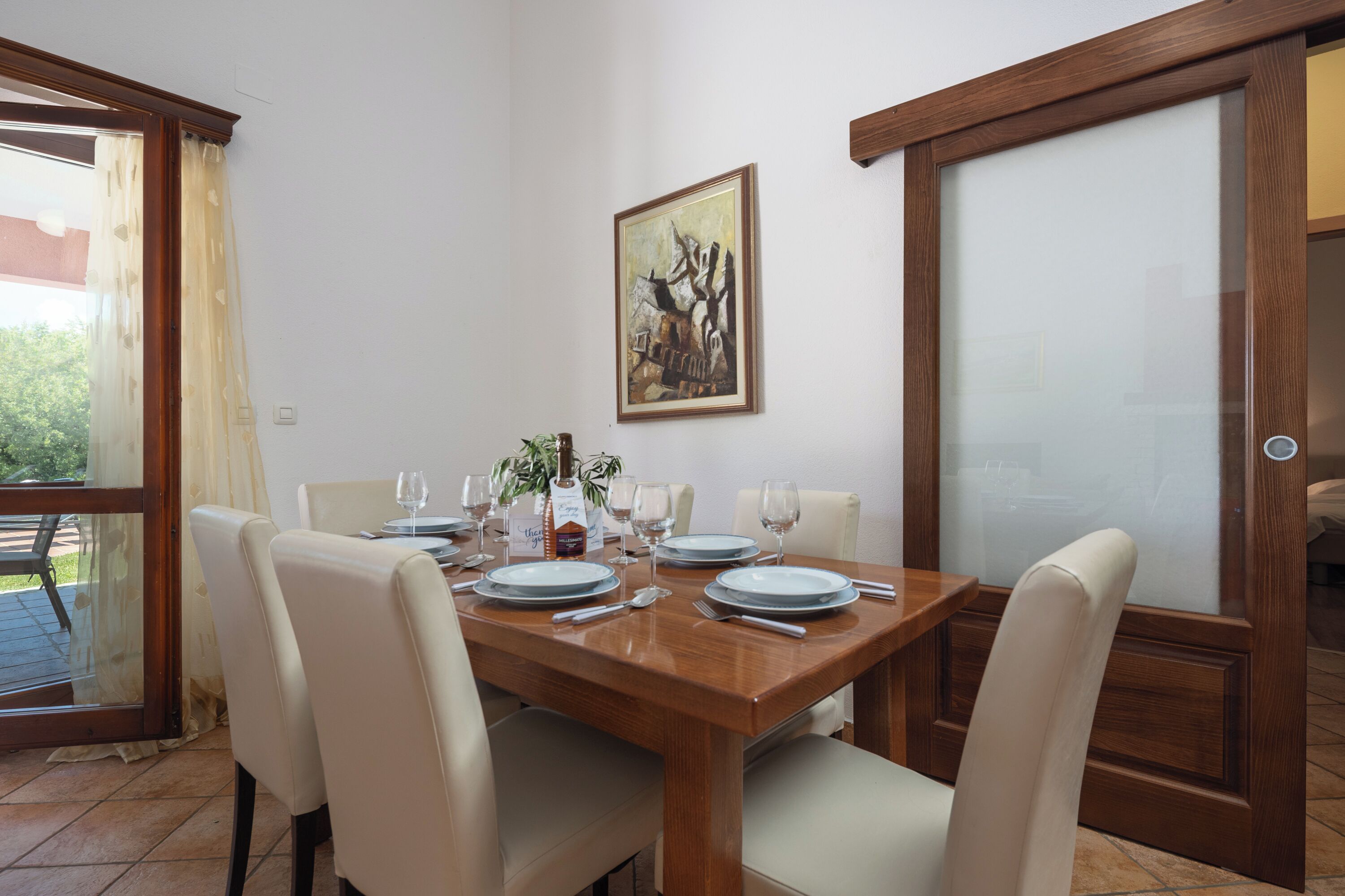 Un coin repas avec une table en bois dressée pour quatre personnes, entourée de quatre chaises. Un tableau est accroché au mur, au-dessus de la table.