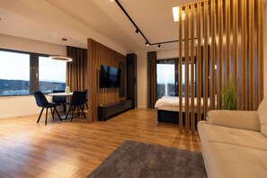 Une chambre d’hôtel moderne dotée d’une grande fenêtre, d’un téléviseur à écran plat, d’un canapé, d’un coin repas et d’un balcon avec vue.