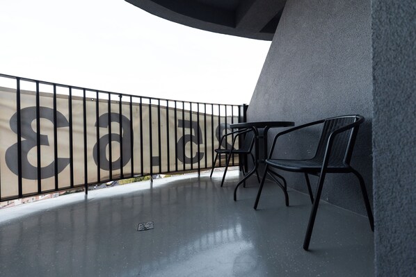 Un balcon avec une balustrade en métal, deux chaises noires et une table.