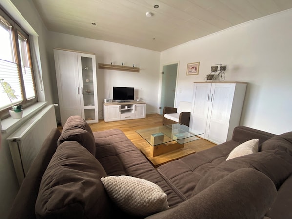 A living room with a brown sofa, a glass coffee table, a TV, and a cabinet.