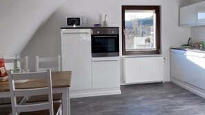 Cocina compacta con armarios blancos, horno integrado, microondas y ventana con vistas al exterior.