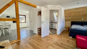 Un interior moderno con suelo de madera, una zona de comedor, una cocina y un dormitorio con cama y una silla roja.