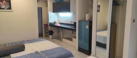 A bedroom with a bed, a small kitchenette, and a bathroom visible through an open door.