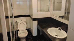 Et badeværelse med toilet, håndvask og en bruseniche med glasvægge.
