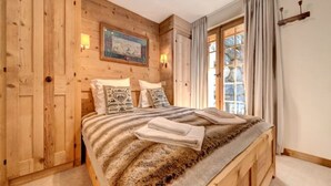 A wooden-paneled bedroom with a bed, pillows, and a window with curtains.