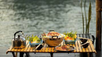 Una mesa de madera con una tetera, un bol grande y diferentes platos, con vistas al agua.